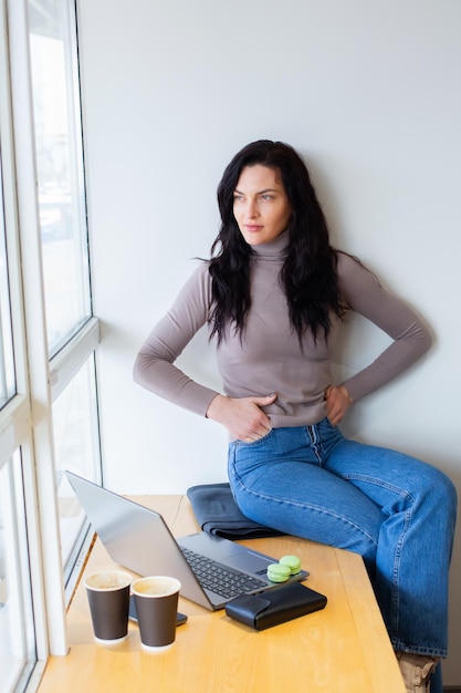 Une femme est assise sur une table avec un ordinateur portable et a mal au ventre.