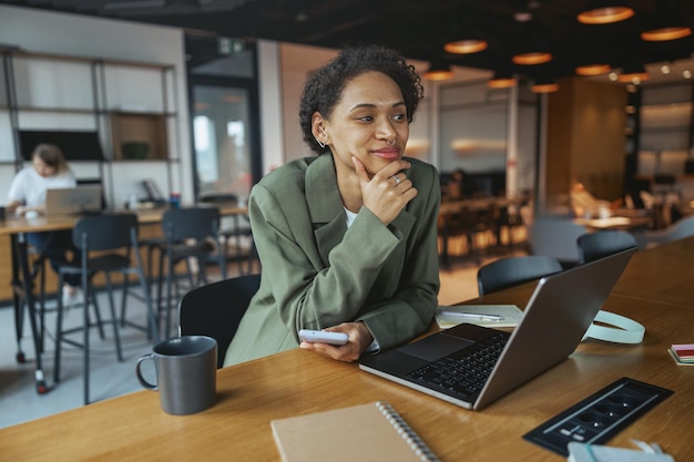 Une femme est assise à une table avec un ordinateur portable et un téléphone portable dans un bureau de coworking moderne et agréable