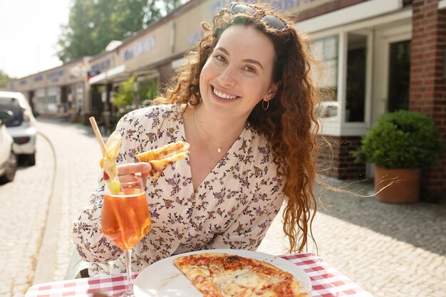 Une femme est assise à une table avec une pizza et un verre de jus d'orange.