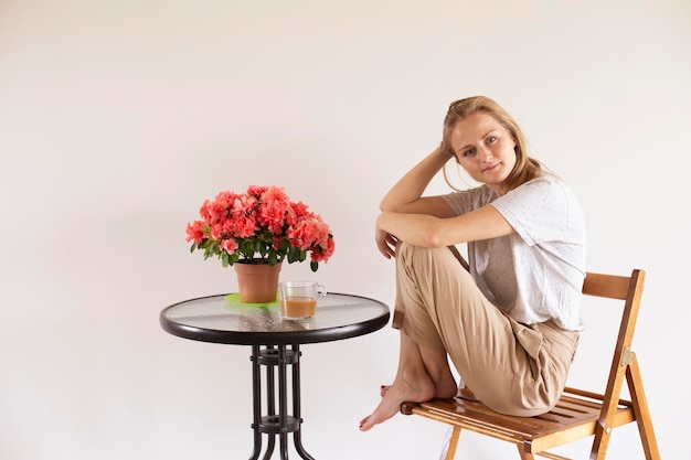 Une femme est assise sur une table avec un pot de fleurs rouges dessus.