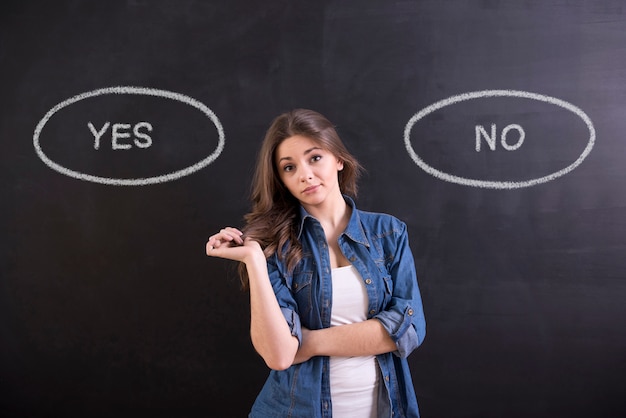 La femme est debout sur un fond noir et pense: oui ou non.