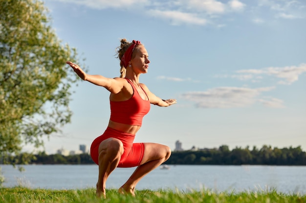 Une femme est engagée dans la gymnastique des flux d'animaux en gros plan à l'extérieur près de la rivière sur l'herbe verte en vêtements rouges