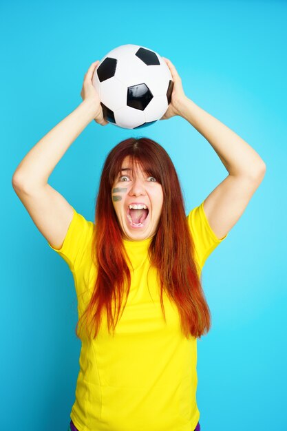 La femme est fan de football en t-shirt jaune avec ballon de football sur fond bleu