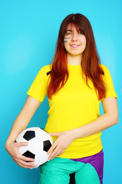 La femme est fan de football en t-shirt jaune avec ballon de football sur fond bleu