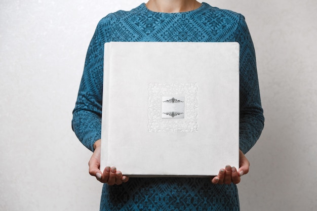 Une femme est titulaire d'un livre photo de famille la personne regarde l'album photo échantillon d'album photo beige dans les mains féminines photoalbum de mariage avec couverture en tissu avec bouclier métallique