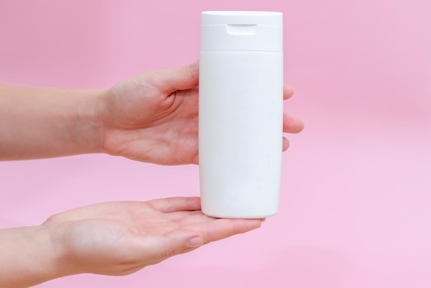 Femme est titulaire d'un shampooing gel lotion crème bouteille blanche pour les produits cosmétiques isolé sur fond rose