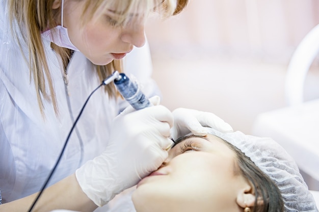 La femme esthéticienne applique le maquillage permanent sur les sourcils de tatouage de sourcils sur de beaux modèles dans un salon de beauté