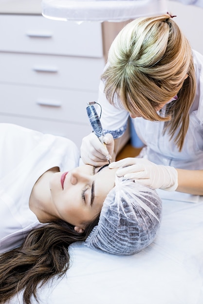 La Femme Esthéticienne Applique Le Maquillage Permanent Sur Les Sourcils De Tatouage De Sourcils Sur De Beaux Modèles Dans Un Salon De Beauté