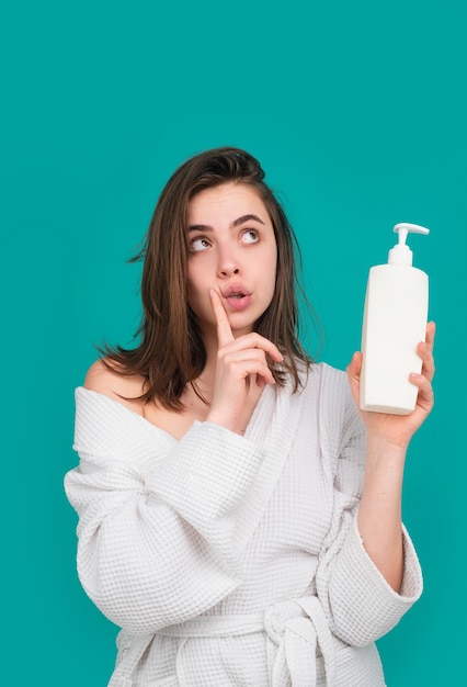 Une femme étonnée tient une bouteille de shampooing et de conditionneur.