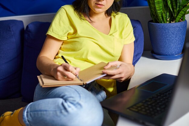 Femme étudiant en ligne à l'aide d'un ordinateur portable, d'un ordinateur portable, écrivant des notes, une femme intéressée écoutant une conférence, regardant un webinaire, apprenant une langue, suivant un cours ou une formation en ligne. Enseignement en ligne à domicile.