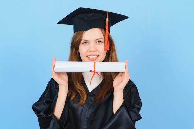 Femme étudiante diplômée portant chapeau et robe de graduation, sur fond bleu