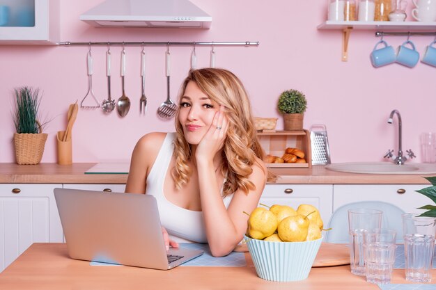 Femme étudiante inquiète et triste à la recherche d'informations dans un ordinateur portable en ligne assis dans la cuisine. Femme blonde triste se sentant stressée à cause de problèmes financiers, travaillant à travers les finances