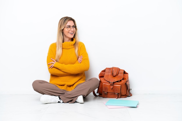 Femme étudiante uruguayenne assis sur le sol isolé sur fond blanc heureux et souriant