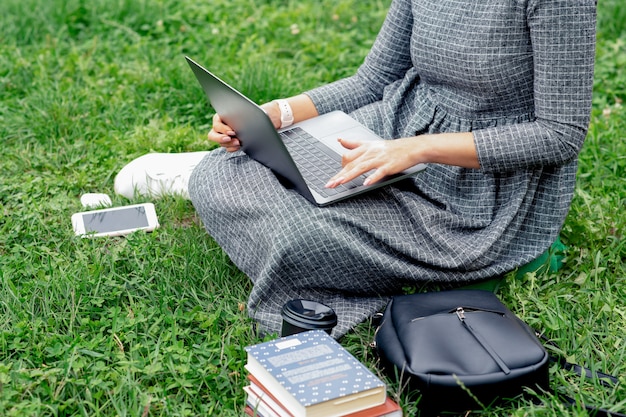Femme étudiante utilise l'ordinateur portable assis sur l'herbe.