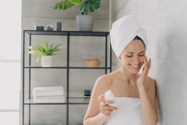 Une femme européenne applique une lotion ou une crème pour le visage à partir d'un flacon et sourit Soin quotidien de la peau