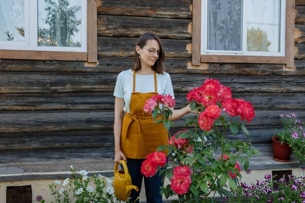 Une femme européenne avec un arrosoir jaune arrose des légumes et des fruits dans son jardin a