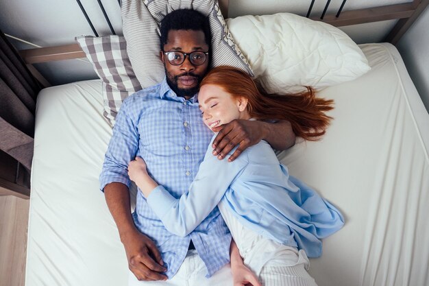 Femme européenne aux cheveux roux et bel homme afro-africain ensemble se serrant dans la chambre à coucher à la maison, appartement confortable.