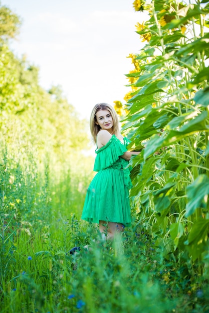 Femme européenne blonde dans une robe verte sur la nature avec des tournesols