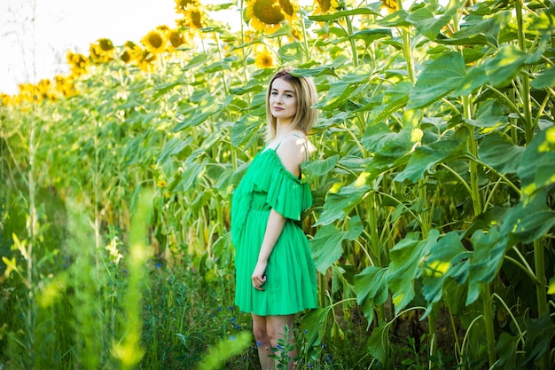 Femme européenne blonde dans une robe verte sur la nature avec des tournesols