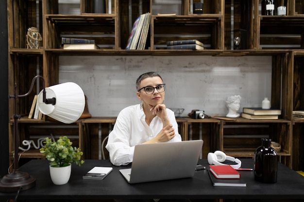 Femme européenne caucasienne élégante sur le lieu de travail dans des verres derrière un ordinateur portable