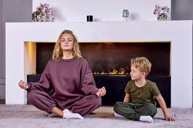 Une femme européenne avec un enfant fait des asanas de yoga à la maison