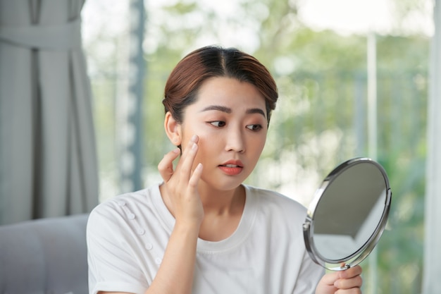 Femme examinant son visage dans le miroir, concept de peau à tendance acnéique problématique