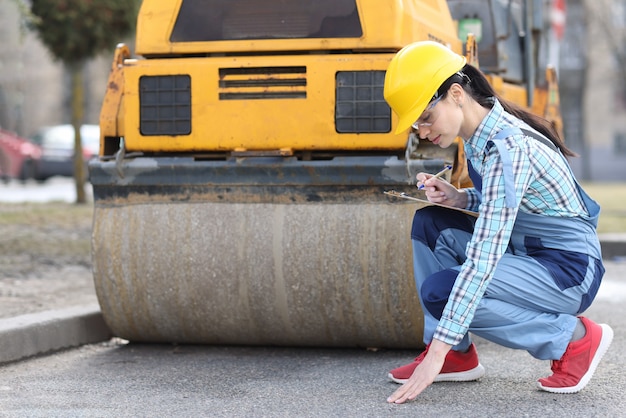 La femme examine la chaussée d'asphalte devant le finisseur d'asphalte