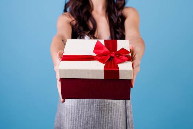 Femme excitée avec une boîte cadeau avec ruban rouge portant une robe isolée sur bleu