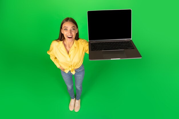 Femme excitée montrant un ordinateur portable avec un écran blanc sur fond vert