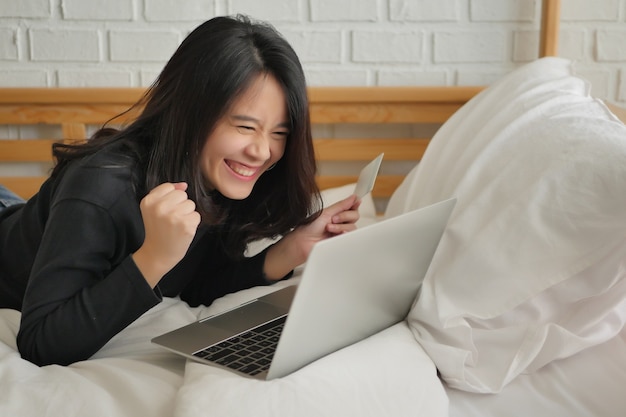 Femme excitée avec ordinateur portable et carte de crédit, concept de magasinage en ligne