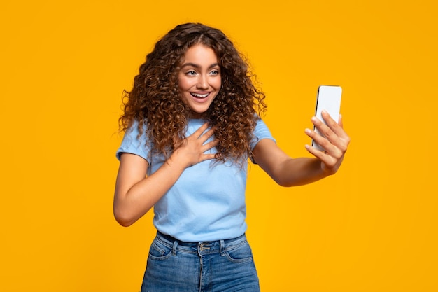 Une femme excitée prenant un selfie avec son smartphone sur jaune