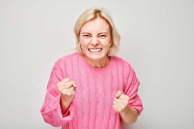 Femme excitée en pull rose serrant les poings dans la victoire ou le succès isolée sur un fond clair