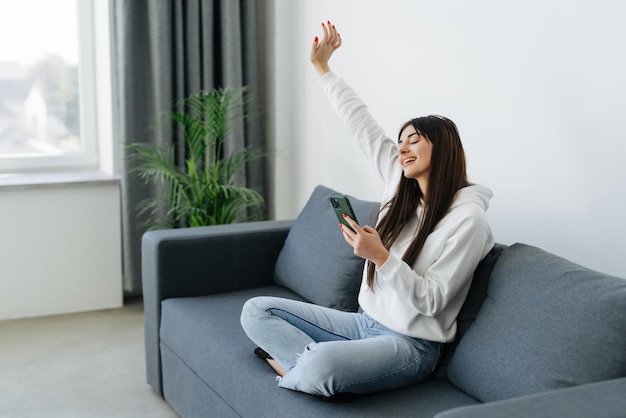 Femme excitée regardant du contenu multimédia en ligne dans un téléphone portable assis sur un canapé dans le salon à la maison
