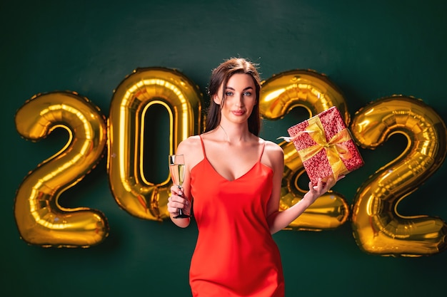 Une femme excitée en robe rouge tient la boîte rouge cadeau et un verre de concept de vacances de fête au champagne