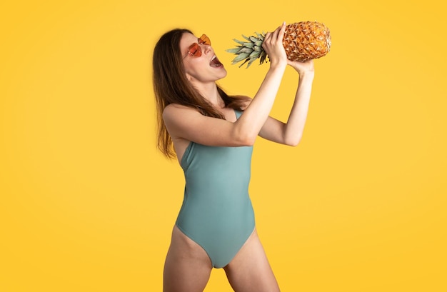 Femme excitée tenant des ananas frais juteux et chantant comme dans un microphone s'amusant et appréciant