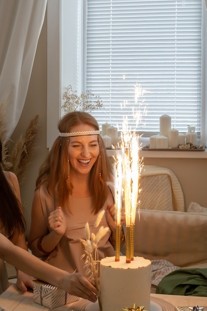 Femme excitée vêtements de mode hippie moderne célébrant son anniversaire avec des coffrets cadeaux gâteau au feu de pétard