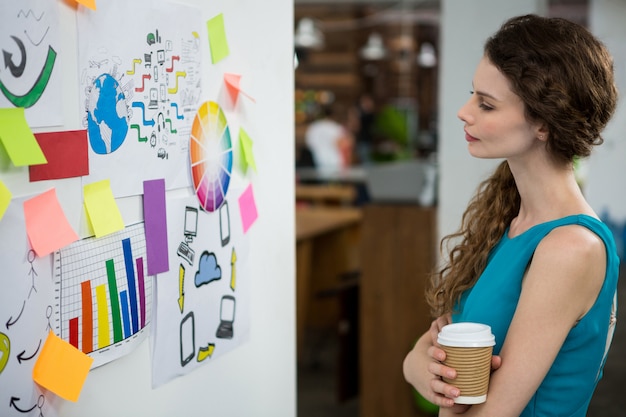 Femme exécutive réfléchie regardant des notes autocollantes sur un mur blanc