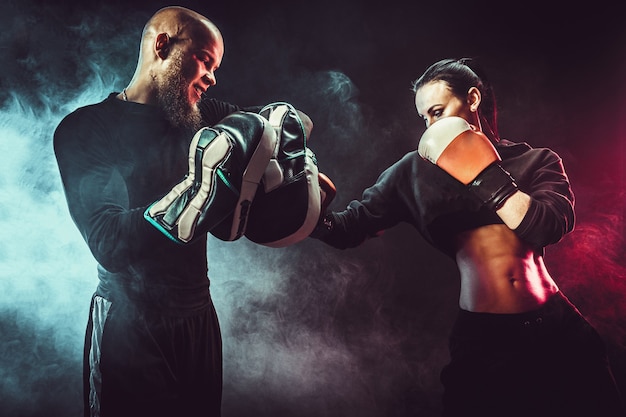 Femme exerçant avec entraîneur à la leçon de boxe et d'autodéfense, studio, fumée sur l'espace