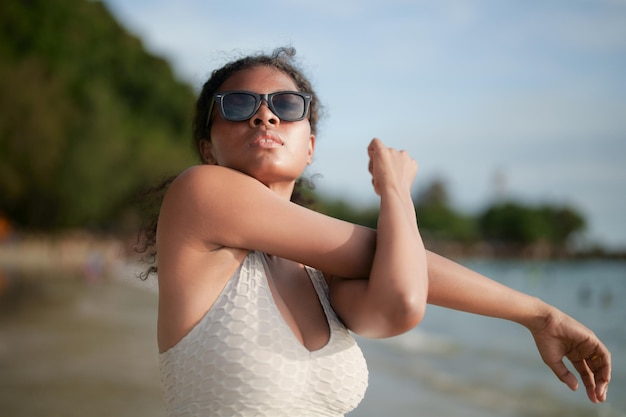 Femme exerce et étire les muscles avant l'entraînement en plein air Portrait sexy femme africaine asiatique se prépare pour le fitness à la plage