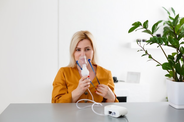 une femme fabrique un nébuliseur par inhalation à la maison. tenant un masque nébuliseur inhalant des vapeurs vaporisez le médicament dans votre patient malade des poumons. auto-traitement des voies respiratoires à l'aide d'un nébuliseur par inhalation