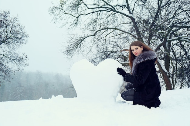 Une femme façonne un grand cœur avec la neige