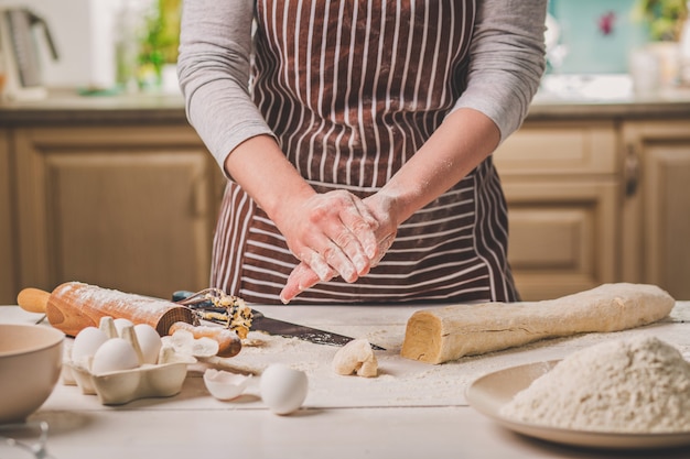 Femme faire des tartes. Le confiseur fait des desserts. Faire des petits pains. Pâte sur la table. Pétrir la pâte. Une femme en tablier rayé cuisine dans la cuisine