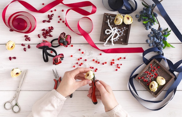 Femme faisant des bijoux, atelier à domicile. Artisan pov, mains féminines créant un accessoire avec des perles et des rubans, vue de dessus. Beauté, créativité, concept d'artisanat