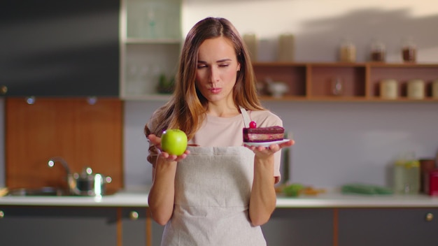 Femme faisant le choix entre pomme et gâteau dans la cuisine