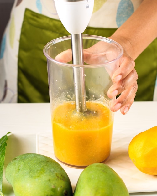 Photo une femme faisant du jus de mangue (smoothies) à l'aide d'un mélangeur à main. mangue ou mangga fruit tropical favori