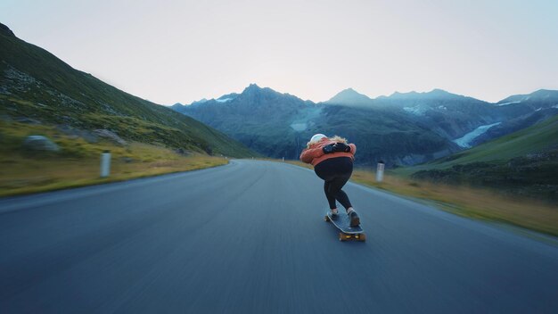 Femme faisant du skateboard et faisant des tours entre les courbes sur un col de montagne