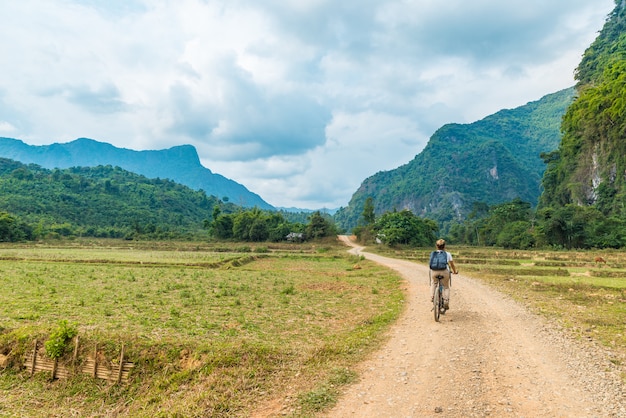 Femme faisant du vélo de montagne sur un chemin de terre dans un paysage pittoresque autour de Vang Vieng, destination de voyage pour routards au Laos