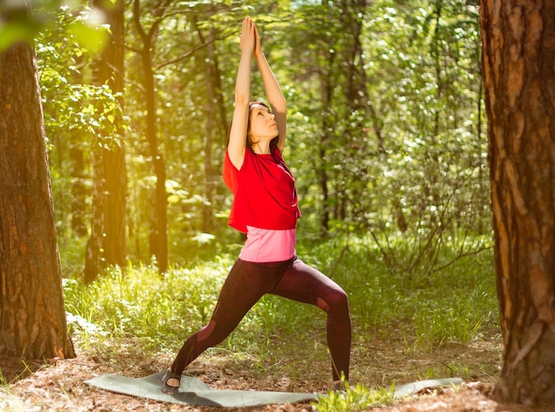 Femme faisant du yoga dans le parc et levant les yeux entouré d'une végétation luxuriante et d'arbres