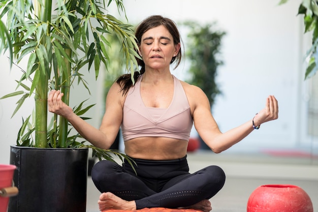 Femme faisant du yoga avec les jambes croisées et les bras levés sur le côté des plantes