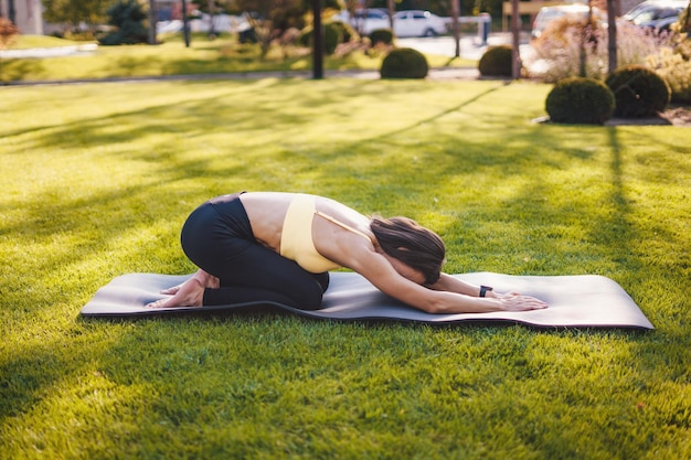 Femme faisant du yoga pose streching atteignant les mains sur un tapis de yoga noir à l'arrière-cour Un exercice facile et un moment de détente à la maison